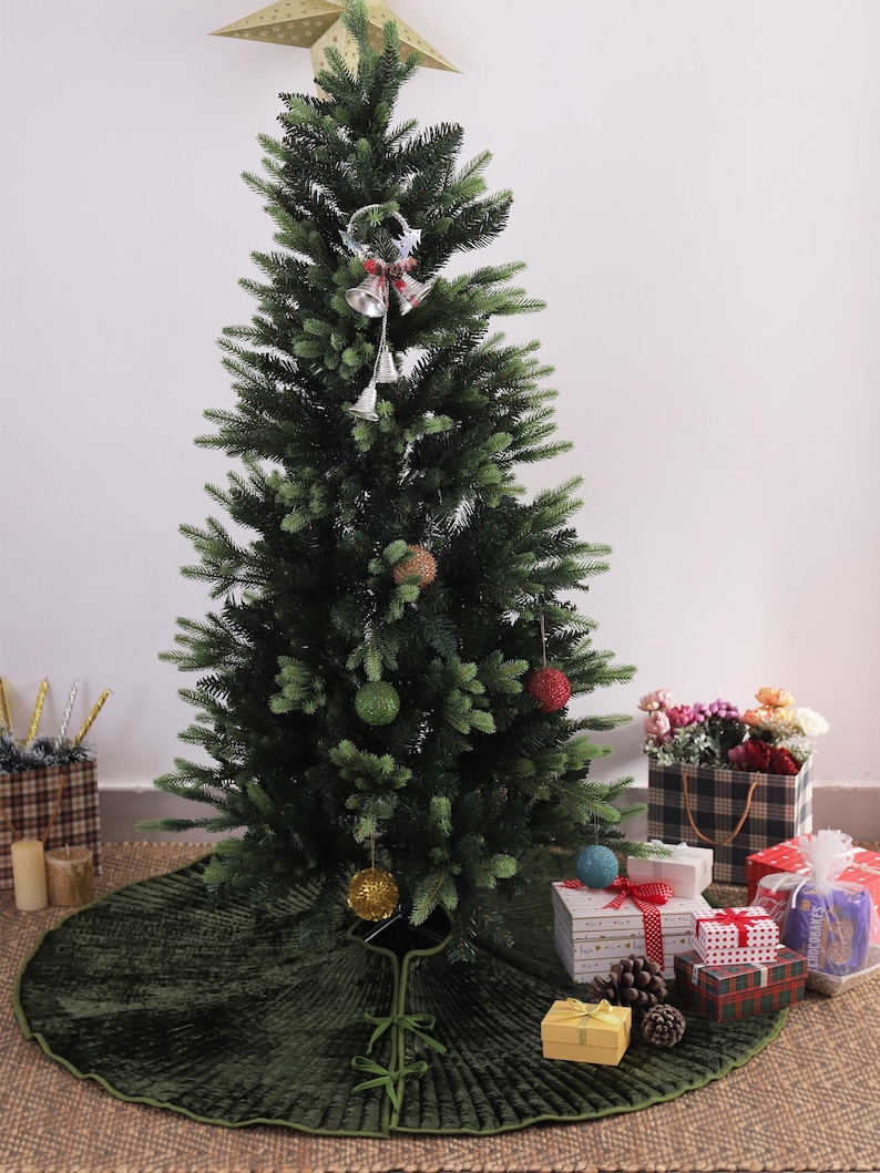 Puede incluir: Un &aacute;rbol de Navidad artificial decorado con una estrella dorada, adornos y campanas plateadas. Una falda de &aacute;rbol verde rodea la base. Regalos envueltos en papel de colores est&aacute;n colocados alrededor del &aacute;rbol, creando un ambiente festivo.