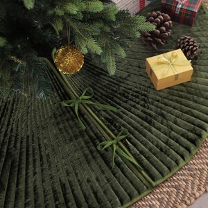 Puede incluir: Una falda de &aacute;rbol de Navidad de terciopelo plisado verde oscuro con un borde verde a juego. La falda est&aacute; decorada con un adorno dorado, una peque&ntilde;a caja de regalo y pi&ntilde;as. La falda tiene aproximadamente 127 cm de di&aacute;metro.