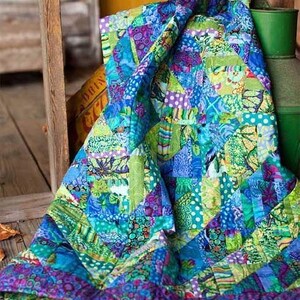 A vibrant, colorful quilt with a patchwork of various patterns and textures, including shades of blue, green, yellow, and purple, is draped over a wooden surface.