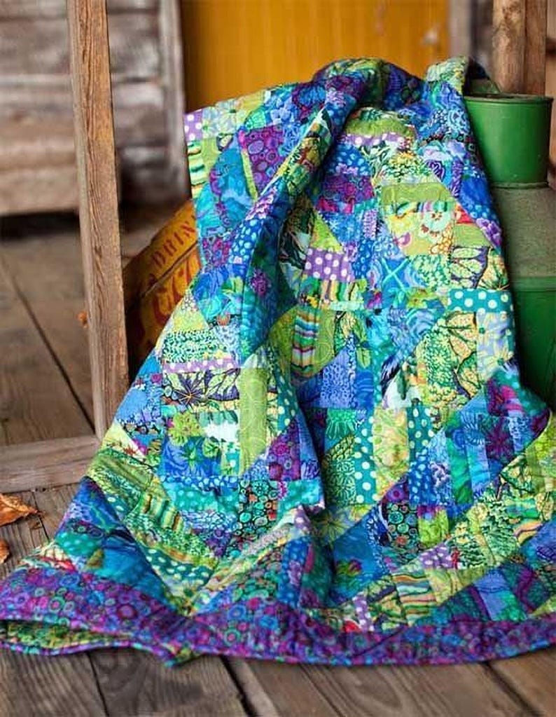 A vibrant, colorful quilt with a patchwork of various patterns and textures, including shades of blue, green, yellow, and purple, is draped over a wooden surface.