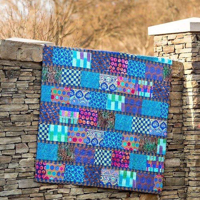A colorful patchwork quilt is hanging on a stone wall, featuring a variety of patterns and textures.