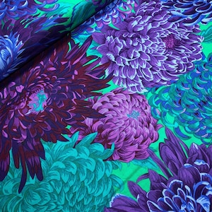 May include: Close-up of fabric with a vibrant floral pattern. Large chrysanthemum blooms in shades of purple, teal, and blue are set against a bright green background. The fabric has a soft, flowing appearance.