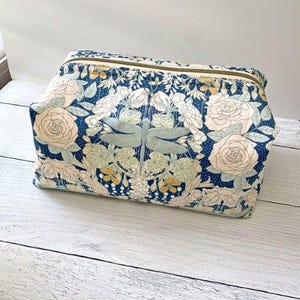A floral print cosmetic bag with a blue and white color scheme, featuring a pattern of roses, leaves, and other flowers.
