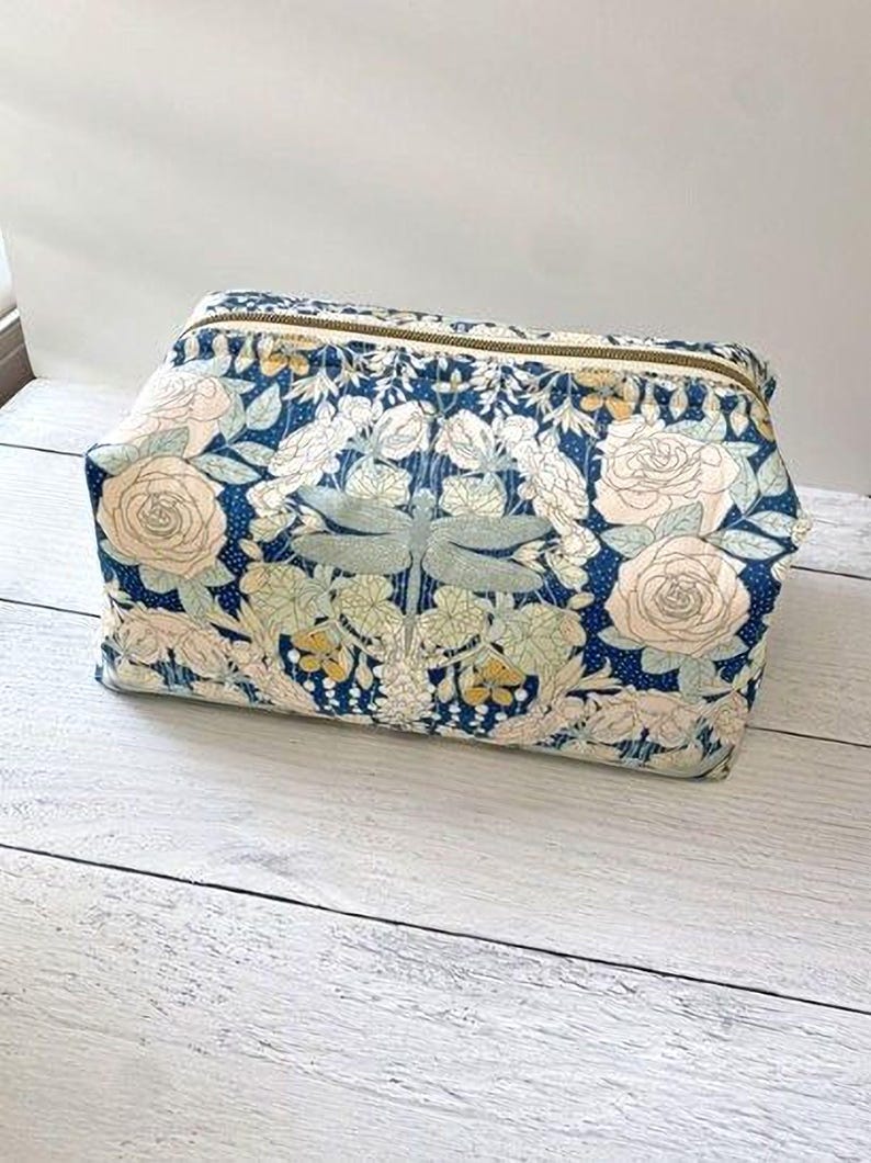 A floral print cosmetic bag with a blue and white color scheme, featuring a pattern of roses, leaves, and other flowers.