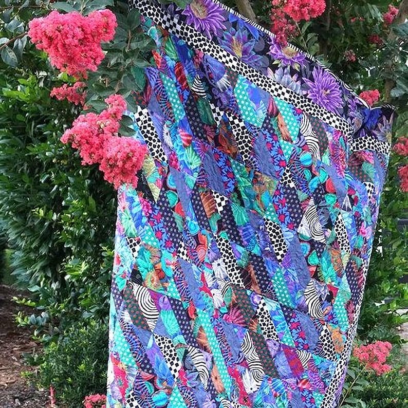 A vibrant, colorful quilt with a patchwork of various patterns and textures, hanging on a tree branch surrounded by pink flowers.