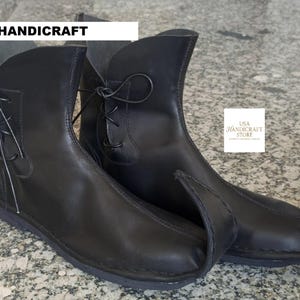 May include: A pair of black leather boots with pointed toes and lace-up details. The boots have a unique, curved design and are likely handmade. The text "USA HANDICRAFT" is visible on the top of the left boot.