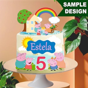Op de afbeelding: Een verjaardagstaart versierd met een cartoon varkensfamilie, een regenboog en een huis. De taart heeft de naam "Estela" en het nummer "5". De taart staat op een witte taartstandaard.