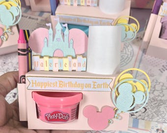 May include: A light pink cardboard desk organizer featuring a castle cutout, a Play-Doh container, and a crayon holder. The front displays the text "Happiest Birthday on Earth" and "Valerieland" with decorative pastel balloon and mouse ear accents.