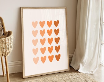 May include: A framed art print featuring a grid of orange hearts in varying shades against a cream background. The artwork is displayed in a light wood frame, leaning against a neutral wall. The overall aesthetic is modern and minimalist.