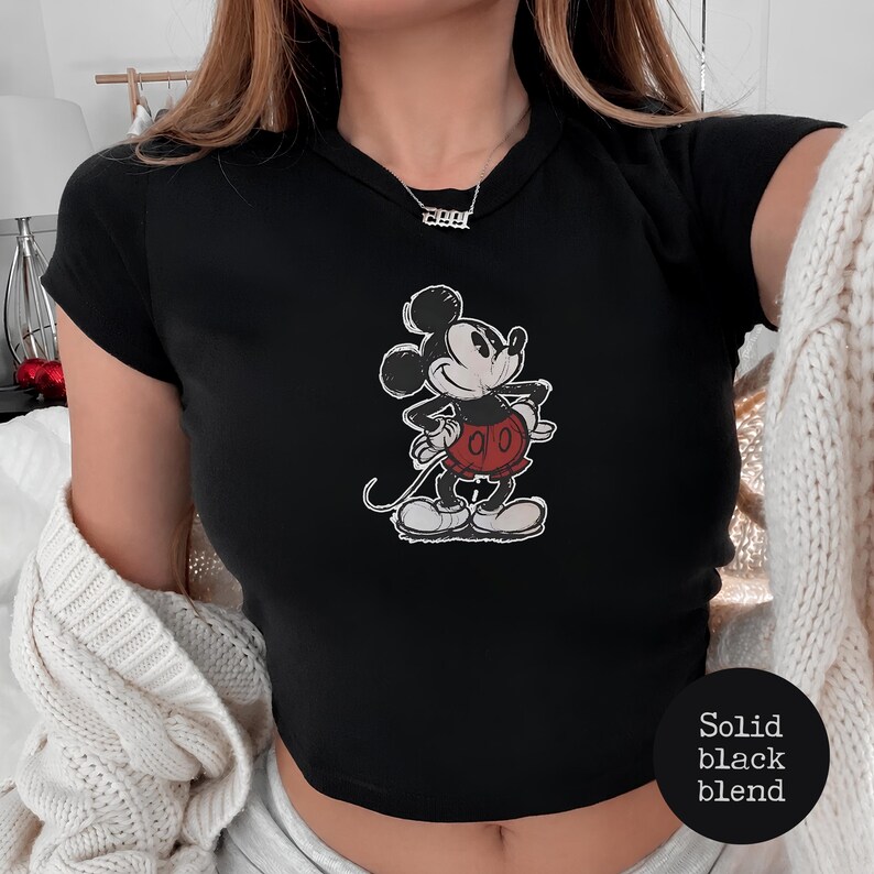 K&ouml;nnte beinhalten: Schwarzes Crop-Top mit einem verblichenen Mickey Mouse-Motiv in Schwarz, Wei&szlig; und Rot. Die Zeichentrickfigur ist in einer klassischen Pose dargestellt. Das Top hat kurze &Auml;rmel und einen Rundhalsausschnitt. Der Text "Solid black blend" befindet sich unten rechts.