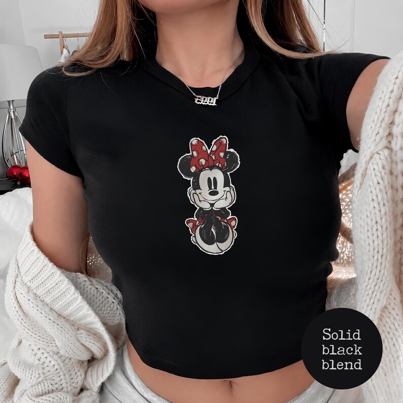 May include: Black crop top featuring a Minnie Mouse graphic with a red bow and polka dots. The shirt has short sleeves and a round neckline. The text "Solid black blend" is on the bottom right.