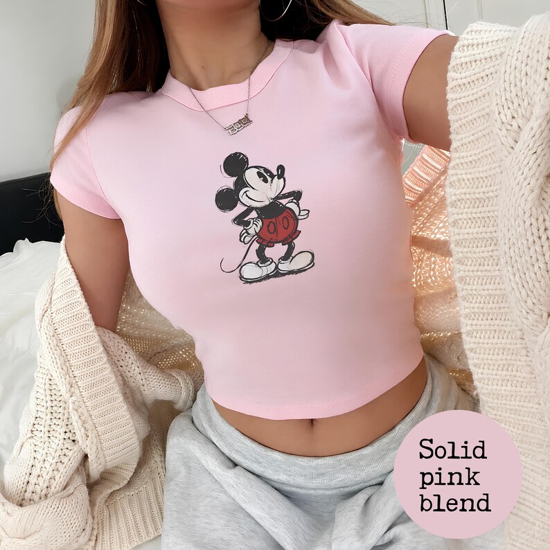 K&ouml;nnte beinhalten: Hellrosa Crop-Top mit Mickey Mouse-Print. Das kurz&auml;rmelige Oberteil hat einen Rundhalsausschnitt und besteht aus einer einfarbigen rosa Mischung. Die Grafik ist in Schwarz, Rot und Wei&szlig;.