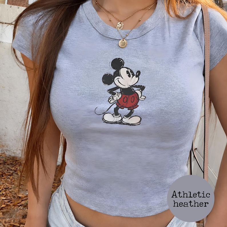 K&ouml;nnte beinhalten: Hellgraues Crop-Top aus Athletic Heather mit einem Mickey Mouse-Motiv. Die Cartoonfigur ist in Schwarz, Rot und Wei&szlig; dargestellt. Das Oberteil hat einen Rundhalsausschnitt und kurze &Auml;rmel.