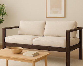 May include: A modern living room scene featuring a two-seater sofa with cream-colored cushions and dark brown wooden frame. A light wood coffee table holds a wooden bowl and books. A potted plant and framed artwork complete the decor.
