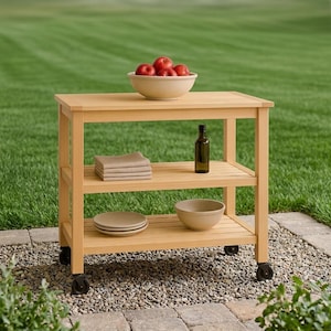 May include: A light-coloured wooden kitchen cart with three tiers and four black caster wheels. The top surface holds a beige bowl filled with red apples. The middle shelf contains a stack of folded beige napkins and a dark glass bottle.