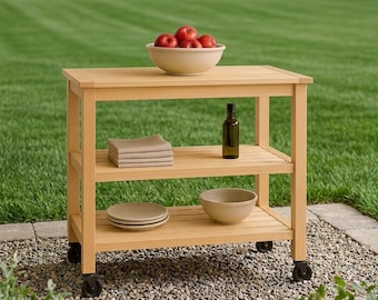 May include: A light-colored wooden kitchen cart with three tiers and four black caster wheels. The top surface holds a beige bowl filled with red apples. The middle shelf contains a stack of folded beige napkins and a dark glass bottle.