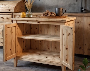 May include: A light-colored wooden cabinet with two doors open, revealing two shelves. The cabinet is part of a rustic kitchen set. A vase with dried plants, a yellow fruit, and a tray with food are on top. The cabinet is made of wood.