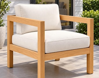 May include: An outdoor armchair featuring a light-toned wooden frame with a square, geometric structure. The chair includes a thick, off-white seat cushion and a matching back cushion, both with piped edges, providing a clean and simple appearance.