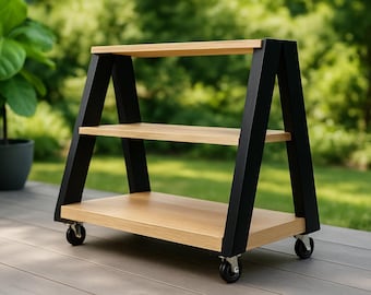 May include: A three-tiered wooden cart with a natural wood finish and black angled supports. The cart has four wheels for easy mobility. The background features a green, blurred outdoor setting.