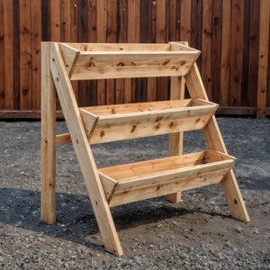 May include: A three-tiered wooden planter with a natural finish. The planter has a ladder-like design with three rectangular planting boxes. The structure is made of light-colored wood and is suitable for outdoor use.