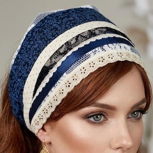 May include: A blue and white patterned headscarf with lace and ribbon accents. The head covering is worn by a person with auburn hair and gold filigree earrings. The headscarf has a floral design.