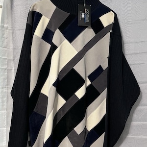 May include: A black, cream, gray, and navy blue patchwork sweater with a high neck and long sleeves. The sweater features a geometric design and a tag that reads "KOMAN". The sleeves are a solid black knit.