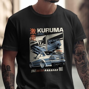 May include: Black t-shirt featuring a car graphic with the text "KURUMA ZUKI" in white and Japanese characters. The design includes illustrations of blue and white cars with the year 1990. The shirt has a crew neck.