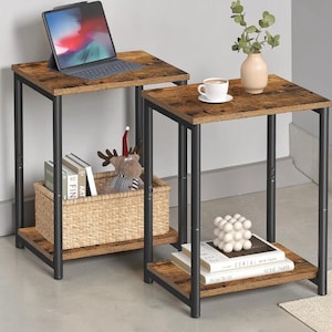 Puede incluir: Juego de dos mesas auxiliares con tapa efecto madera rústica y patas de metal negro. Una mesa tiene una cesta con libros y un reno de peluche. La otra tiene una taza de café, un jarrón y esferas decorativas. Ideales para salón o dormitorio.
