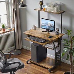 May include: A computer desk with a brown wood-look surface and black metal frame. It features a pull-out keyboard tray, a shelf for the computer tower, and a top shelf. A computer monitor, keyboard, and mouse are on the desk. The desk is on wheels.