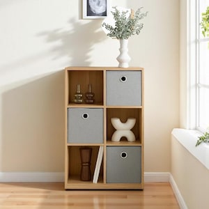 Op de afbeelding: Een houten opbergunit met zes kubussen, grijze stoffen bakken en decoratieve items. De unit heeft een lichte houten afwerking en is gevuld met vazen, boeken en een witte sculptuur. De bakken hebben een ronde handgreep.