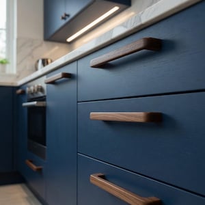 May include: A modern kitchen design featuring navy blue cabinets with wooden drawer pulls. The countertop is a light marble with a warm-toned wooden trim. The kitchen has a built-in oven and a window in the background.