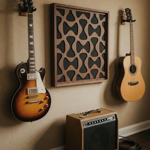 Può includere: Una chitarra elettrica sunburst, una chitarra acustica in legno naturale, un amplificatore per chitarra color cuoio e un pannello acustico da parete quadrato in legno con un motivo scuro ritagliato. Gli strumenti sono montati sulla parete.