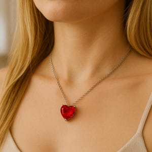 Può includere: Collana con catena d'argento e un grande ciondolo rosso a forma di cuore. Il ciondolo è sfaccettato e cattura la luce, creando un effetto scintillante. Un gioiello semplice ed elegante.
