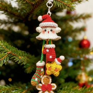 May include: A crocheted Christmas decoration featuring a Santa Claus figure with a red hat and white beard, plus a red mitten, yellow star, green stocking, and gingerbread man. The ornament hangs on a Christmas tree.