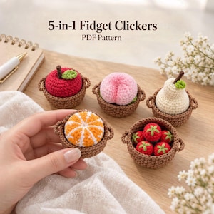 May include: A PDF pattern titled 5-in-1 Fidget Clickers featuring five crocheted fruit items in brown baskets: a red apple, a pink peach, a cream pear, an orange segment, and a basket of red strawberries with green stems and leaves.