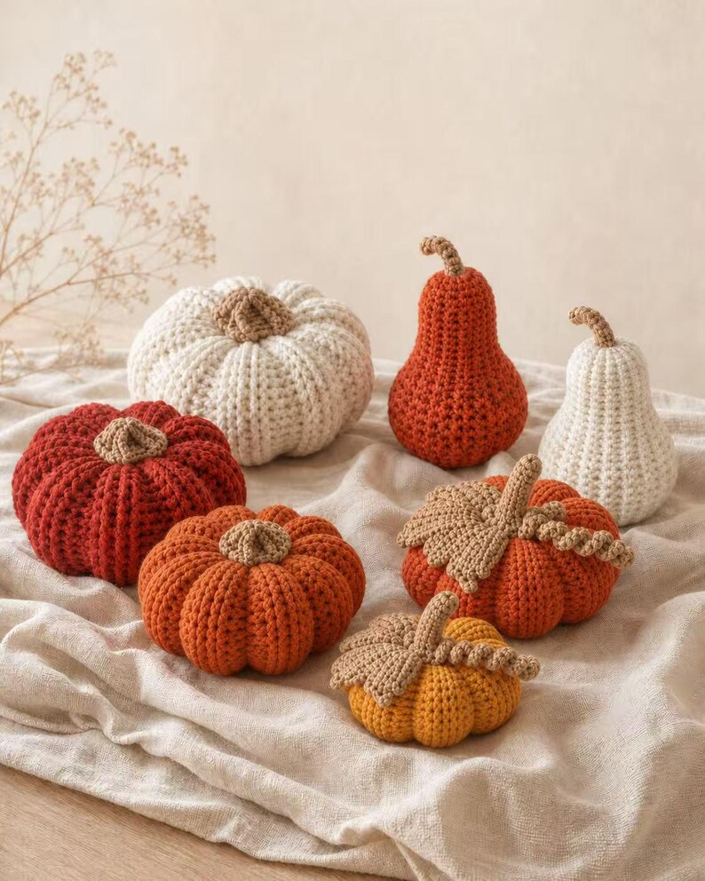 May include: A collection of seven handmade crochet pumpkins and gourds in various sizes and shapes. The set includes items in shades of cream, burnt orange, and mustard yellow, each featuring a textured crocheted stem and some with leaves.