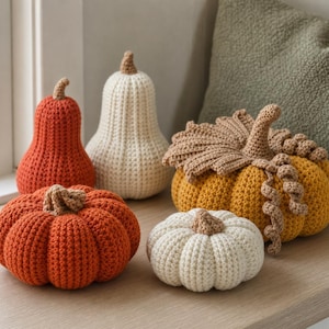 May include: A collection of five handmade crochet pumpkins in various shapes and sizes. The set includes two tall gourd-shaped pumpkins in orange and cream, two round pumpkins in orange and cream, and one large golden-yellow pumpkin with crochet leaves.