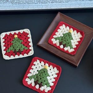 Può includere: Tre sottobicchieri quadrati all'uncinetto con un motivo ad albero di Natale. Ogni sottobicchiere presenta un albero verde con un tronco marrone, una stella gialla e un bordo rosso. I sottobicchieri sono fatti a mano.