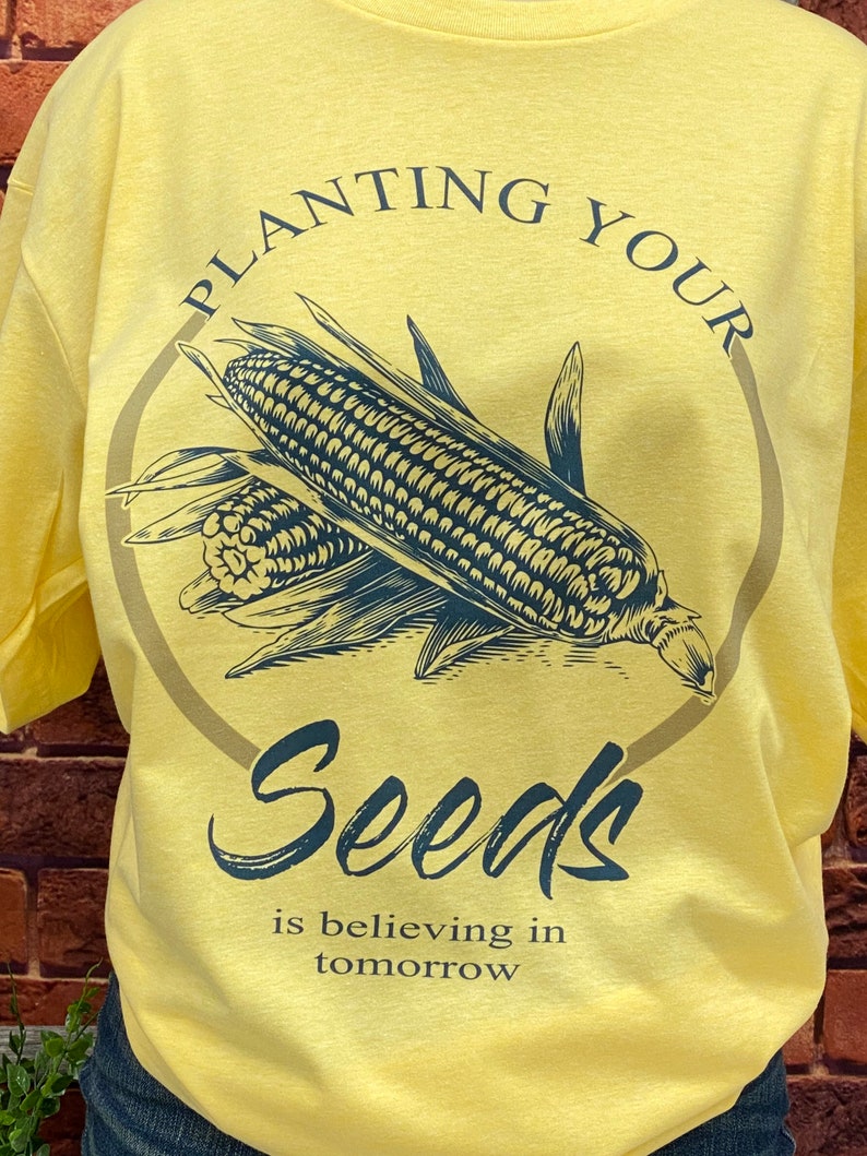 May include: Yellow t-shirt with a black and white illustration of corn and the text "Planting Your Seeds is believing in tomorrow".