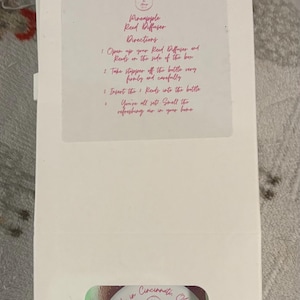 May include: A rustic wooden sign with the text "Welcome" in a handwritten style. The sign is painted white with a distressed finish, and features a decorative floral element in the corner. The background is a blurred image of a wooden surface.