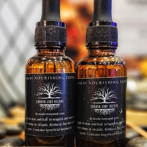May include: Two amber glass bottles of facial serum with black droppers. Each bottle has a black label with white text that reads "AKNI NOURISHING ELIXIR" and "CHAHTA LADY BLENDS". The bottles are on a wooden surface.
