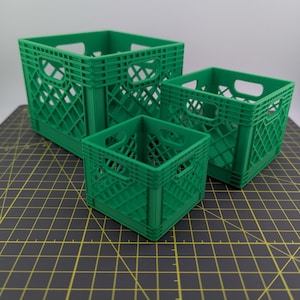 May include: Three green plastic storage crates in the style of milk crates, in different sizes. The crates have a diamond pattern and handle cutouts. The smallest crate is square, the others are rectangular.