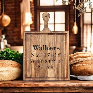 May include: A wooden chopping board with a handle, engraved with the name "Walkers" and coordinates. The board is rectangular with a groove around the edge. The text "N 21° 15' 45.8" W 50° 83' 21.6" - Ruth, Kyle -" is also engraved.
