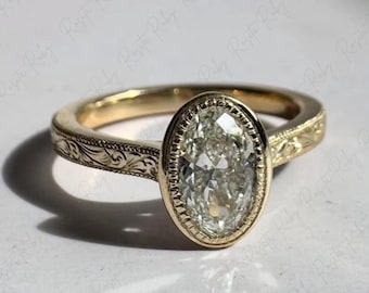 May include: A gold ring with an oval-shaped, clear gemstone. The ring has an engraved floral design on the band and around the gemstone setting. The ring is set against a white background.