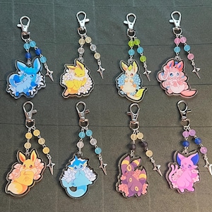 May include: A collection of eight acrylic keychains featuring various cartoon characters. Each keychain has a silver clasp, beaded accents in different colors, and a star charm. The characters are in shades of blue, yellow, pink, and purple.