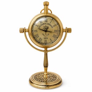 May include: A gold-toned desk clock with a round face and Roman numerals. The clock face displays "Victoria London 1876" and features an anchor and ship's wheel design. The clock is supported by a decorative stand, a classic timepiece.