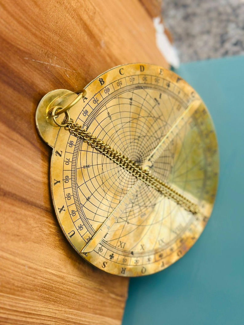 May include: A vintage brass astrolabe with intricate markings and a chain. The circular instrument features a rotating dial with degree markings and a central pointer. The astrolabe is a historical astronomical instrument.