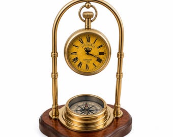 May include: A decorative desk clock and compass set. The clock has a gold-coloured frame and a yellow face with Roman numerals. The compass is set in a gold-coloured base, all on a dark wooden base. The clock face reads 'Victoria London 1915'.