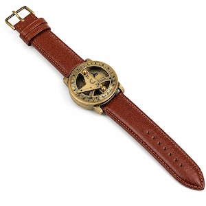 May include: A vintage-style watch with a compass design. The watch has a bronze-coloured face with intricate detailing and a brown leather strap. The strap has a buckle closure and is approximately 24 cm long.