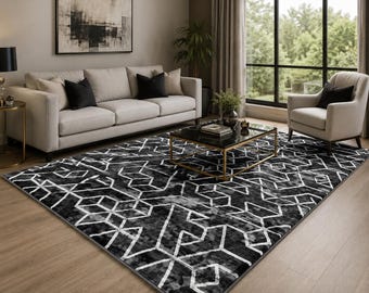May include: A rectangular area rug featuring a high-contrast black and white geometric pattern with interconnected lines and angular shapes. The rug has a textured, mottled appearance and is positioned on a light-colored wooden floor.